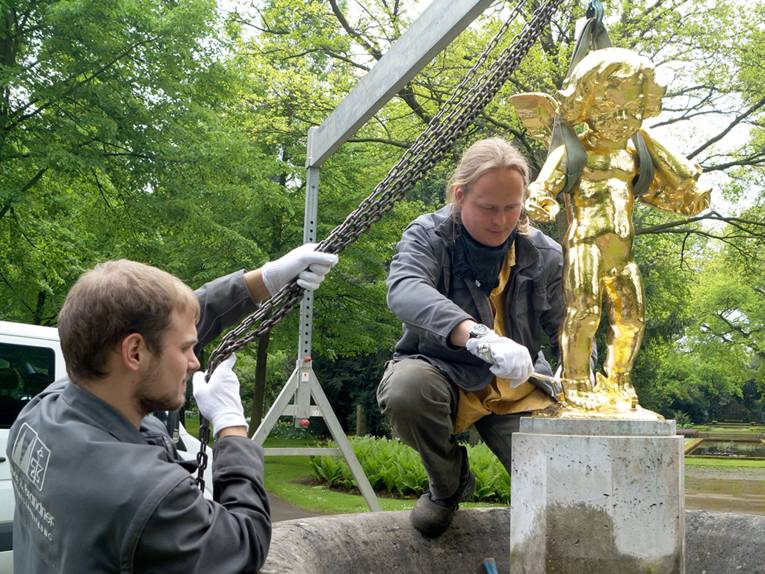 Zwei Männer platzieren eine goldene Statue auf einem steinernen Sockel
