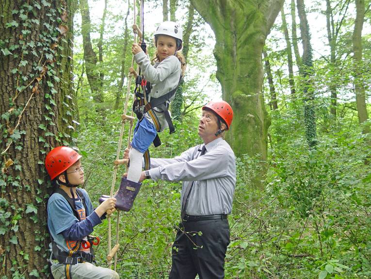 Unterstützt von Harald Härke und einem Jungen klettet ein Mädchen eine Strickleiter an einem Baum hoch