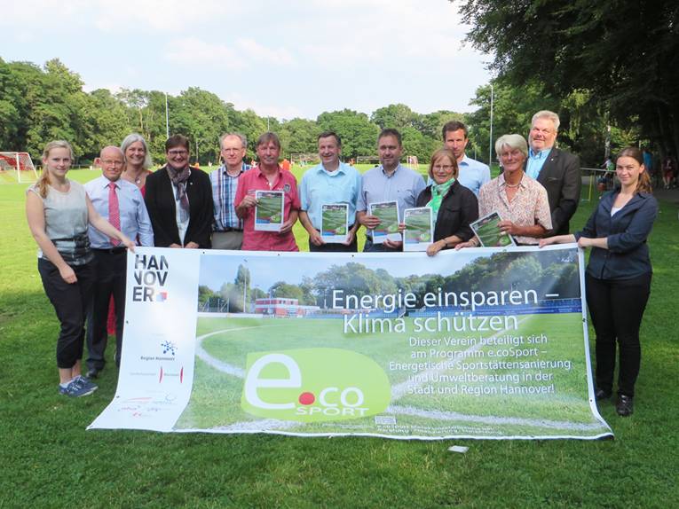 13 Personen stehen auf einem Fußballplatz und halten ein Banner zum e.coSport-Projekt in den Händen