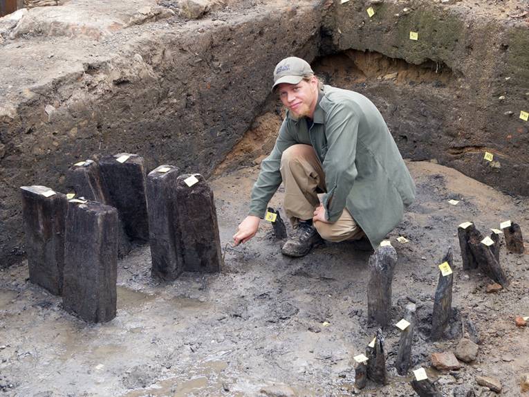 Ein Mann hockt an einem freigelegten Eichenpfahl aus dem Mittelalter