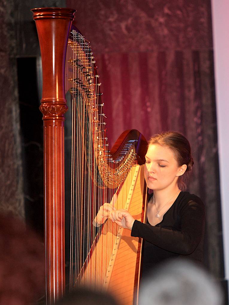 Eine junge Frau spielt vor Publikum Harfe