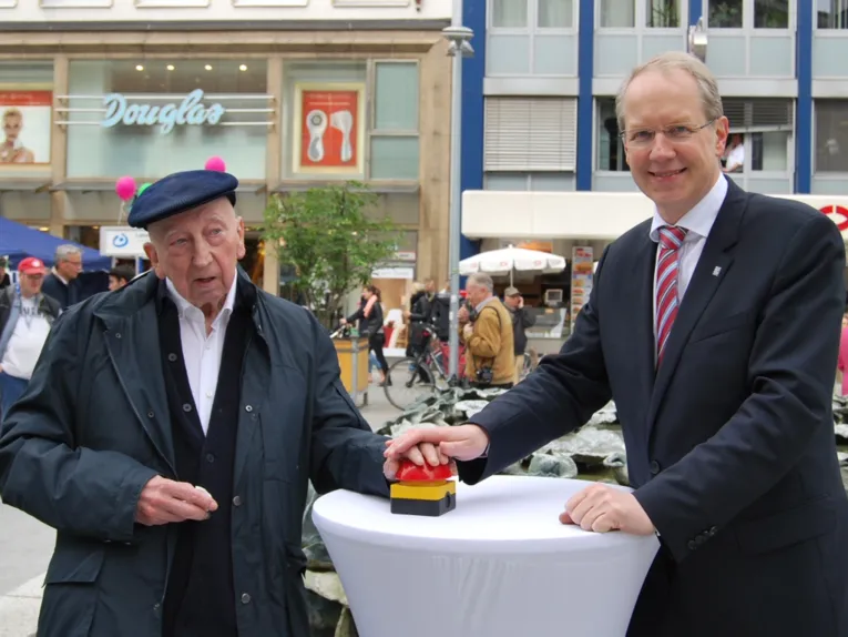 Emil Cimiotti und Stefan Schostok drücken gemeinsam einen roten Knopf, um den Blätterbrunnen wieder in Betrieb zu nehmen