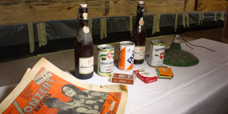 Verscheidene Gegenstände (Bierflasche, leere Zigarettenschachteln und eine Konzertzeitung) aus früheren Zeiten