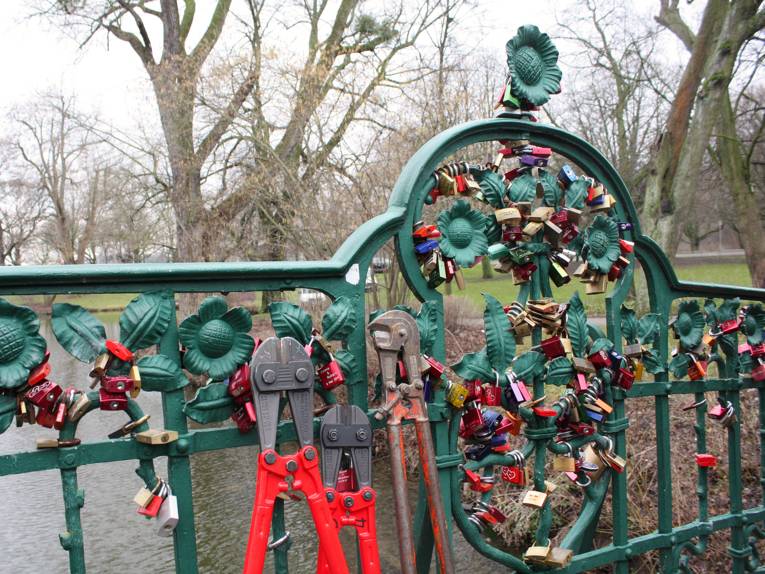 Drei Bolzenschneider lehnen an der schmiedeeisernen Brücke im Maschpark, die mit Liebesschlössern bestückt ist.