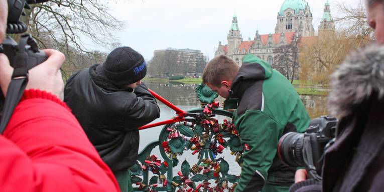 Zwei städtische Mitarbeiter entfernen mit Bolzenschneidern die Vorhängeschlösser an der schmiedeeisernen Brücke im Maschpark.