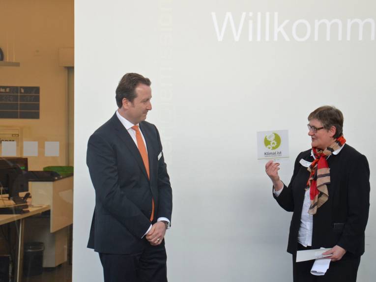 Sabine Tegtmeyer-Dette überreicht BMW-Niederlassungsleiter Uwe Wegener ein Schild mit dem neu gestalteten Logo "KlimaList"