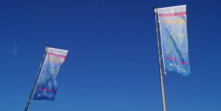 TERRE DES FEMMES-Flaggen, die mit einer Frauenfigur und dem Slogan "frei leben – ohne Gewalt" bedruckt sind