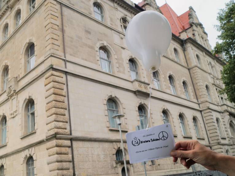 Eine Hand hält einen mit Helium gefüllten Luftballon, an dem eine Postkarte hängt
