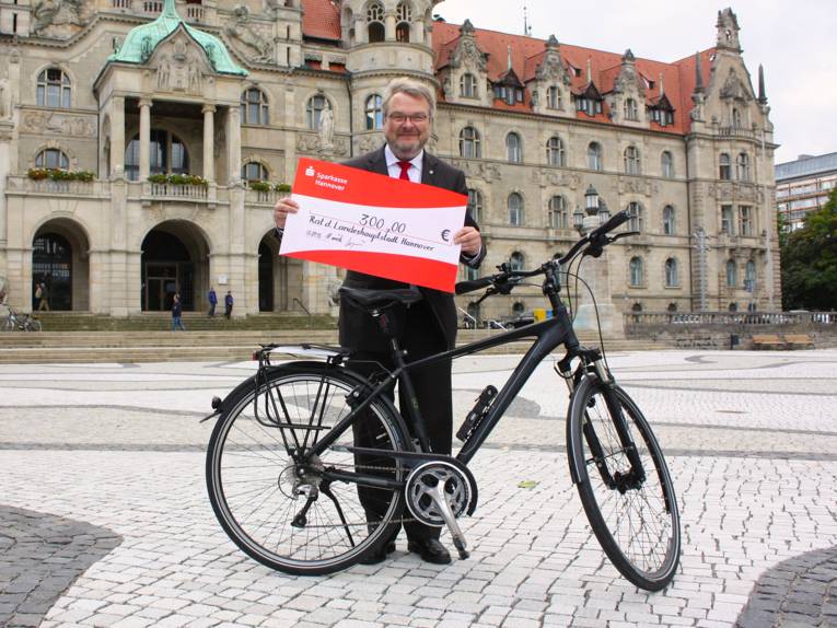 BM T. Herrmann steht mit seinem Rad auf dem Trammplatz und hält einen symbolischen Scheck in die Kamera