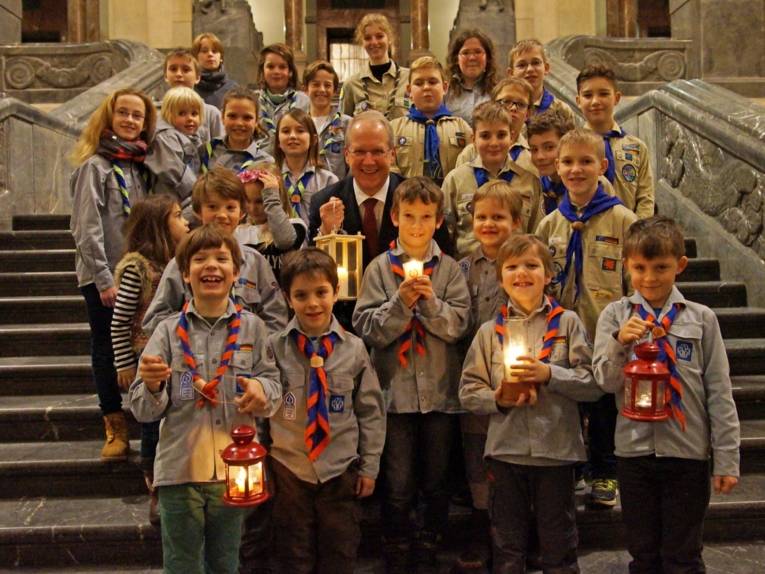 Junge Pfadfinderinnen und Pfadfinder mit Laternen in einer Halle. 