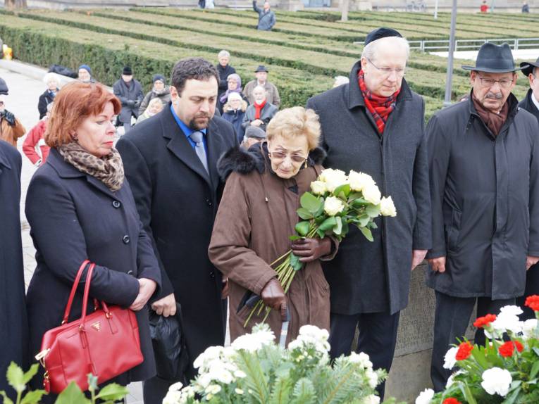 Zwei Frauen und drei Männer vor einem Mahnmal mit Blumen.