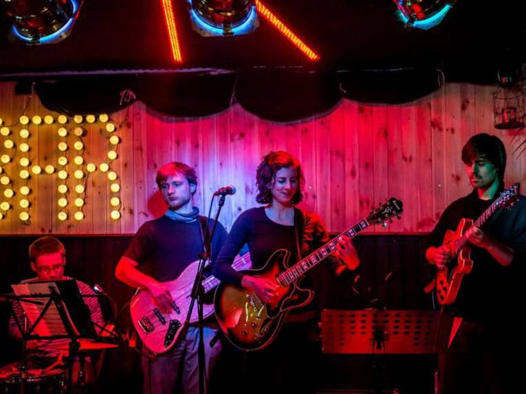 Drei junge Männer und drei junge Frau auf einer bunt beleuchteten Bühne. 