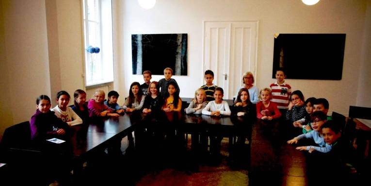 Eine Schulklasse und eine Erwachsene am Tisch. 