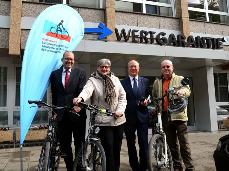 Drei Männer und eine Frau mit Fahrrädern. 