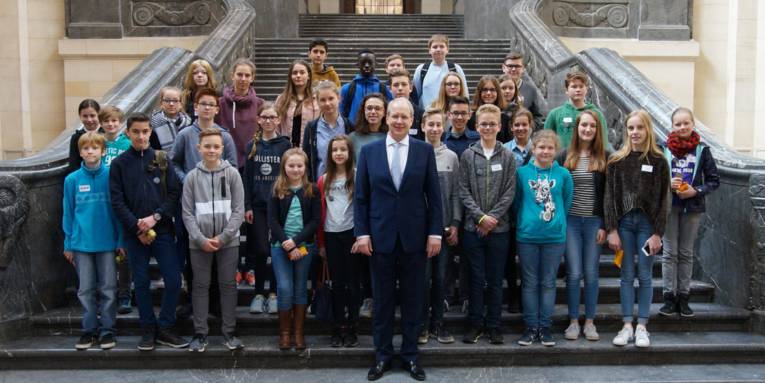 Mann und viele Kinder auf einer Treppe in einer Halle. 