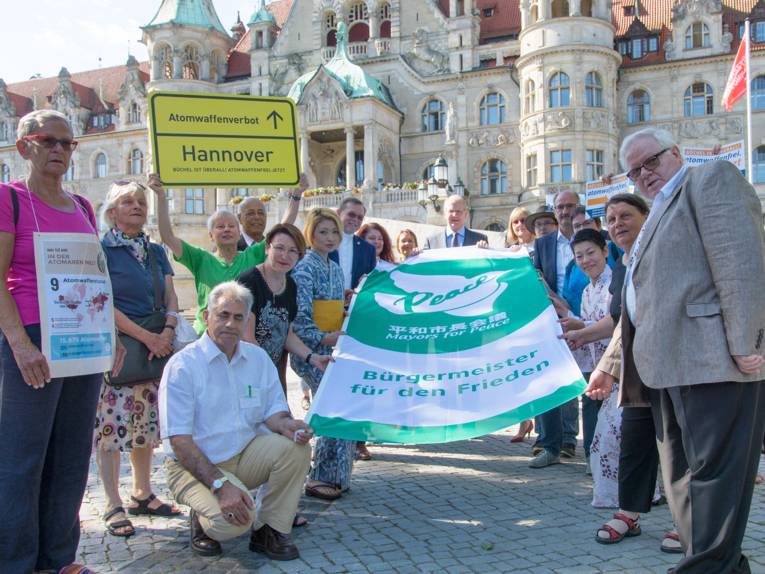 Vor dem Neuen Rathaus präsentiert eine Gruppe Menschen die Flagge der Mayors for Peace