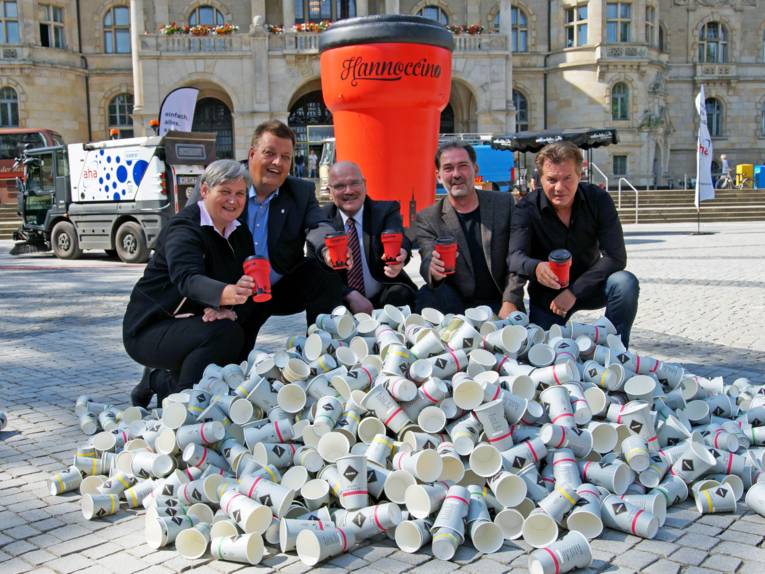 Eine Frau und vier Männer hinter einem Berg aus leeren Coffee-to-go-Bechern.