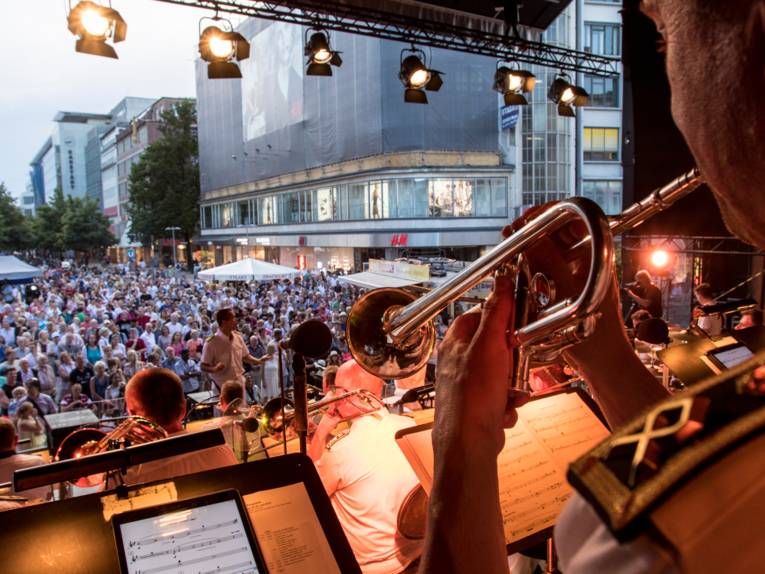 Musikerinnen und Musiker auf einer Bühne. Davor Tausende Menschen. 