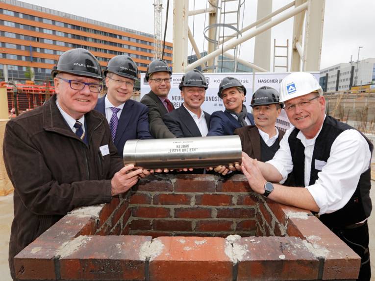 Sieben Männer mit einem Edelstahlzylinder auf einer Baustelle. 