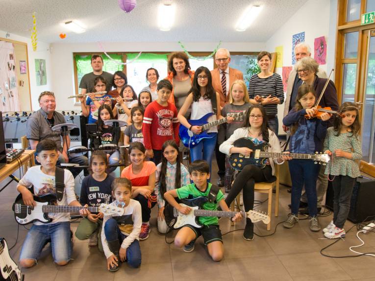 Eine größere Gruppe Kinder sowie einige Erwachsene in einem Raum voller Musikinstrumente
