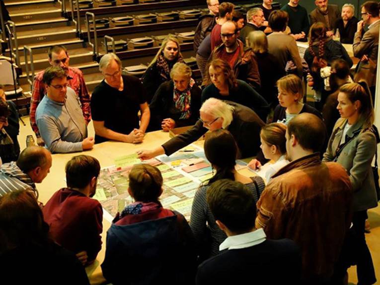 Eine Gruppe Menschen, die um einen Tisch sitzen und auf einen Stadtplan blicken. 