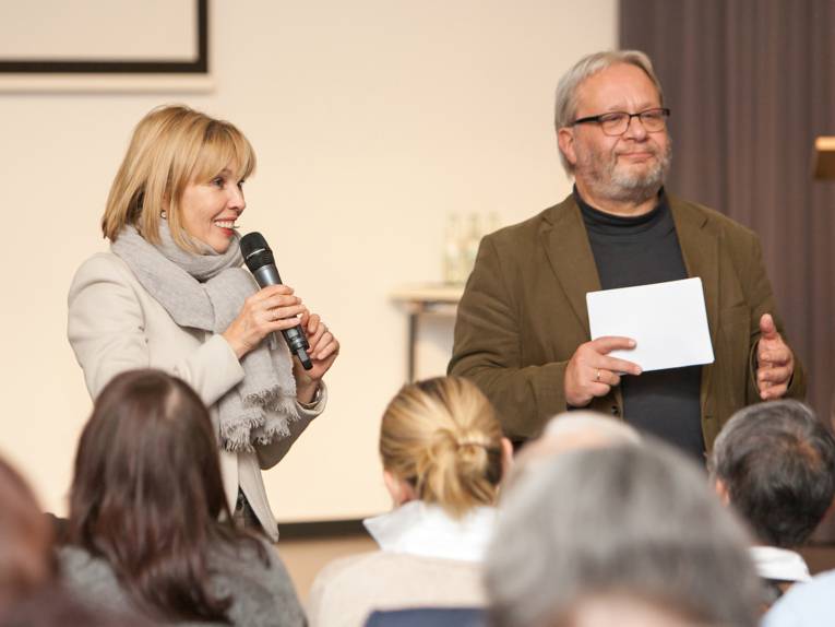 Eine Frau und ein Mann im Dialog mit anderen Menschen. 