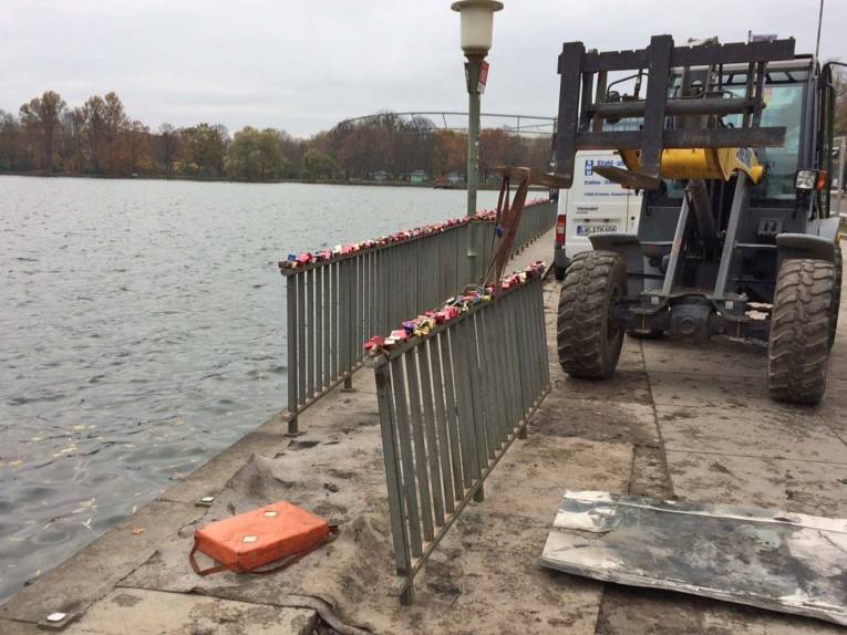 Bagger, der ein Geländer um einen See entfernt hat. 