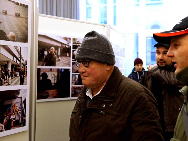 Männer vor einer Ausstellungswand mit Fotografien. 