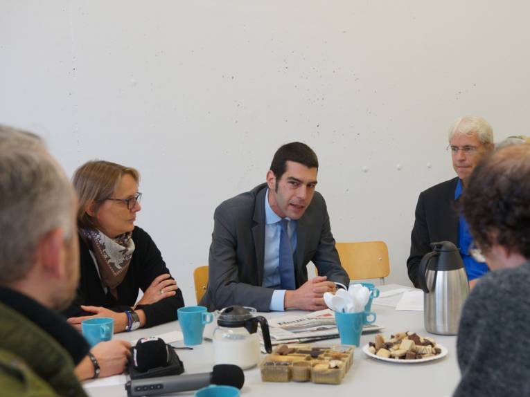 Eine Frau und zwei Männer vor Pressevertretern. 