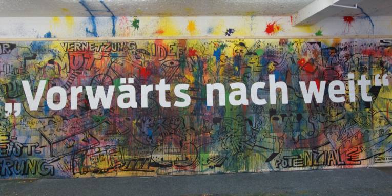Eine Wand voll mit künstlerischen Zeichnungen und dem Spruch "vorwärts nach weit" in weißen Buchstaben darauf. 