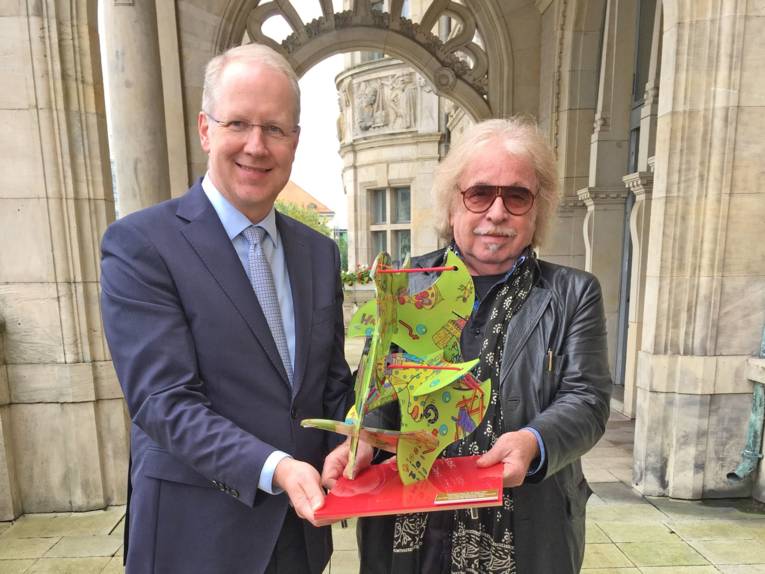 Ein Mann und ein weiterer Mann halten vor sich eine abstrakte Skulptur. 