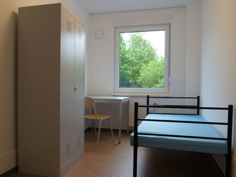 Zimmer mit einem Bett, einem Schrank, einem Tisch und einem Stuhl. 