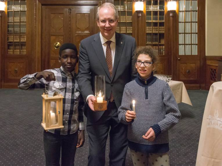 Zwei Kinder und ein Erwachsener mit dem Friedenslicht von Bethlehem