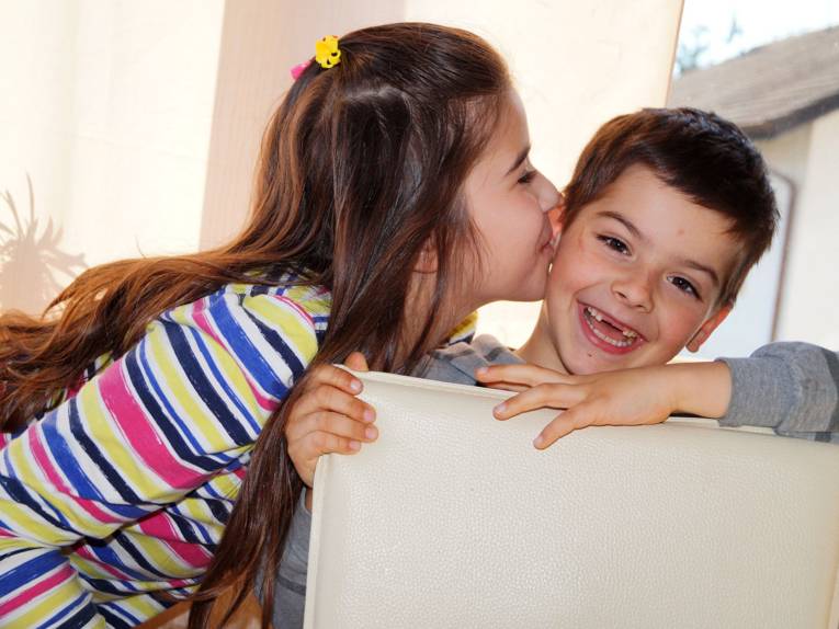 Zwei Kinder in häuslicher Umgebung: Die Schwester gibt ihrem Bruder einen Kuss.