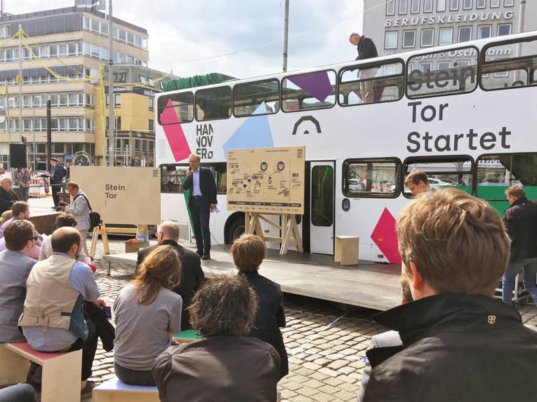 Menschen vor einem Doppeldeckerbus in der Innenstadt. 