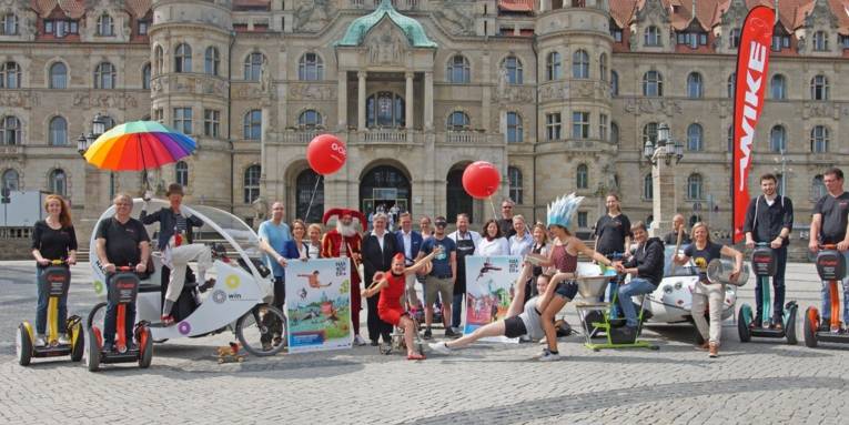 Menschengruppe mit Fahrrädern, Plakaten und Wagen auf einem Platz. 