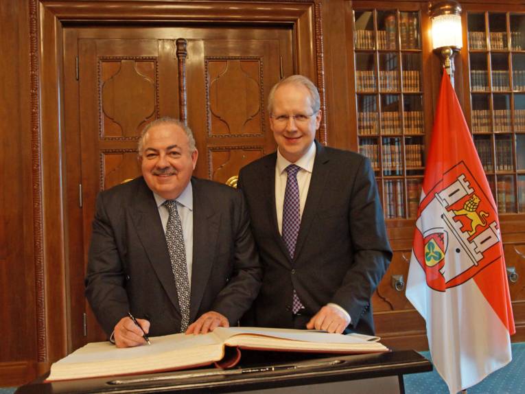 Zwei Männer hinter einem Stehpult. Auf dem Pult liegt ein Buch, in das einer der Männer mit einem Kugelschreiber schreibt. 