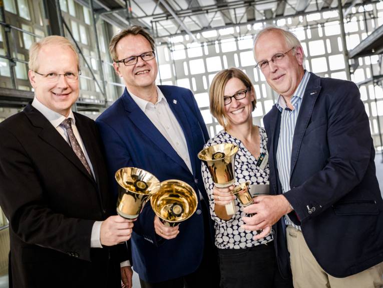 Eine Frau und drei Männer mit Glocken in einem Gebäude. 