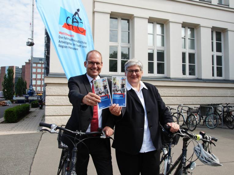 Ein Mann und eine Frau mit Fahrrädern. Sie zeigen einen Flyer. 