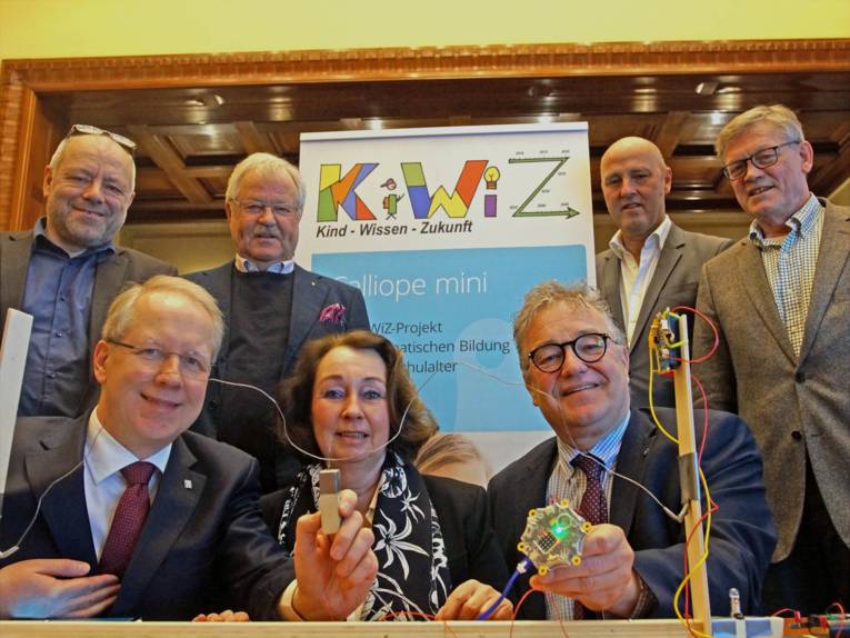 Sieben Männer und eine Frau vor Aufstellern. 