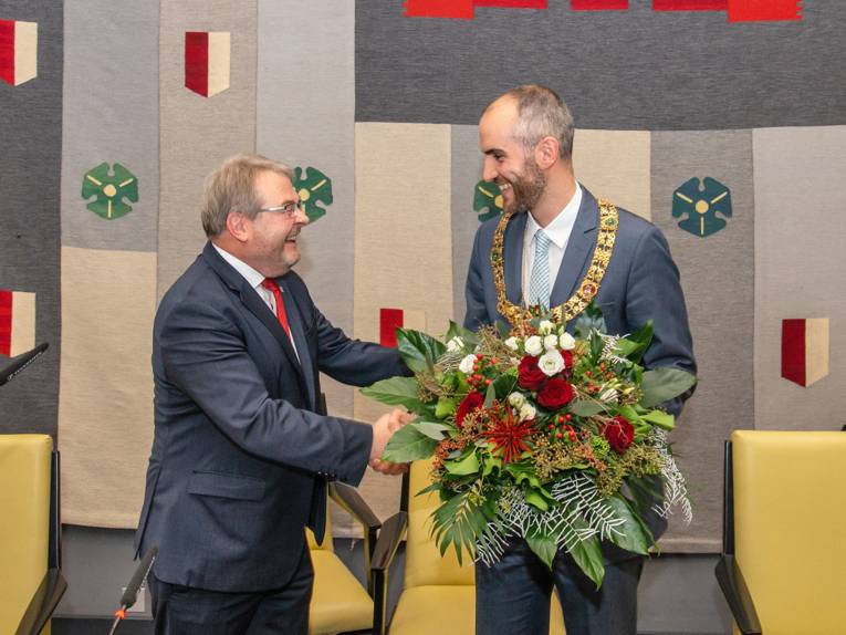 Zwei Männer geben sich die Hand, einer hält zusätzlich einen Blumenstrauß in der anderen