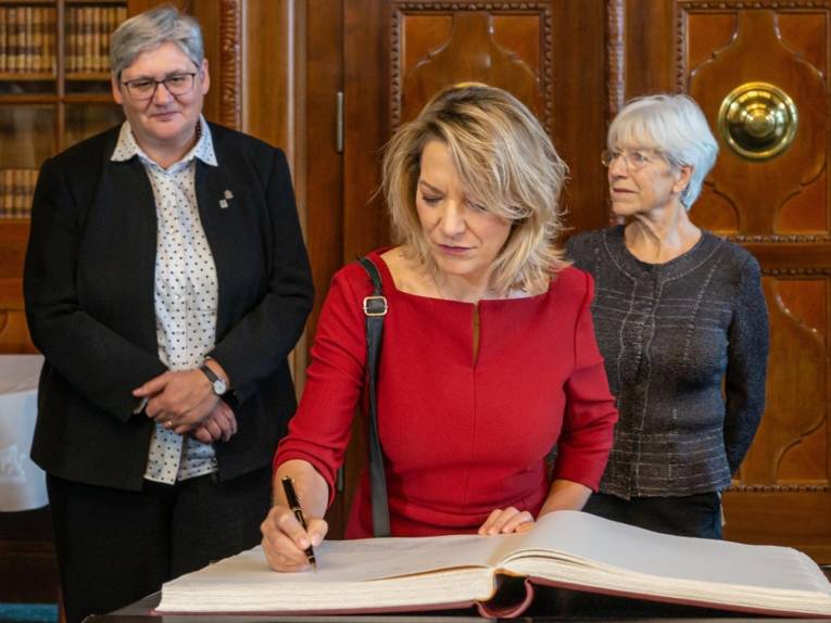 Drei Personen um ein Buch. Eine trägt sich ein. 