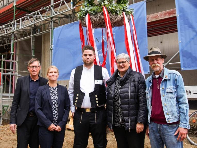 Fünf Personen unter einem Kranz. Im Hintergrund eine Baustelle. 