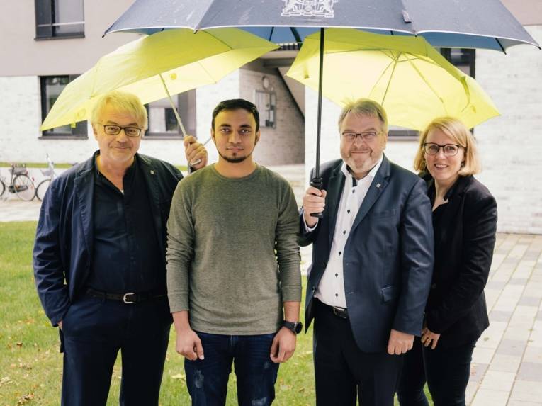 Drei Männer und eine Frau unter Regenschirmen. 