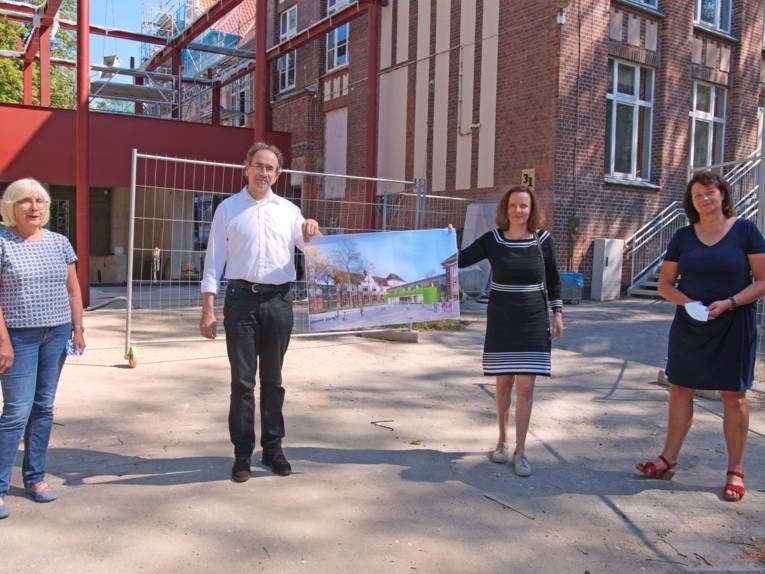 Vier Personen auf einem Hof. Sie halten ein Bild, das eine Schule zeigt. 