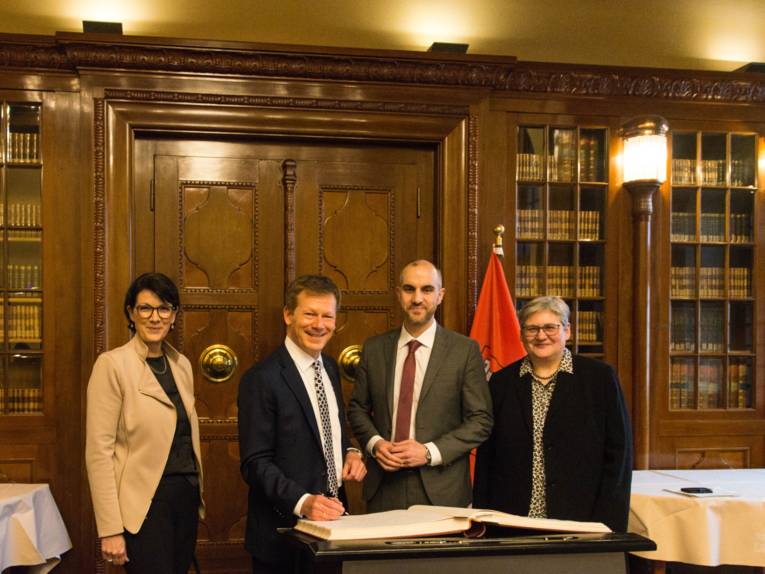 Zwei Frauen und zwei Männer in einem Raum vor einem Buch. 