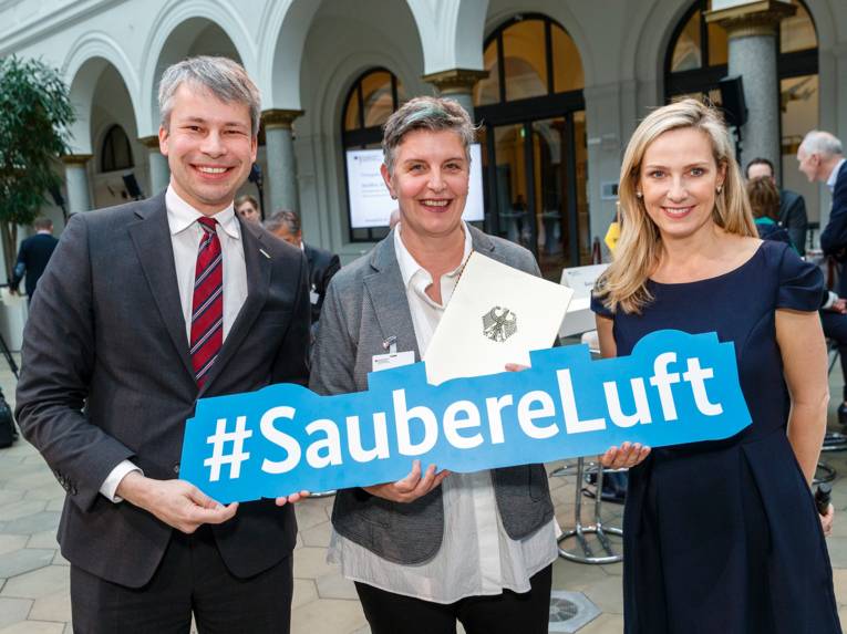 Drei Personen, die ein Schild halten, auf dem "Saubere Luft" steht. 