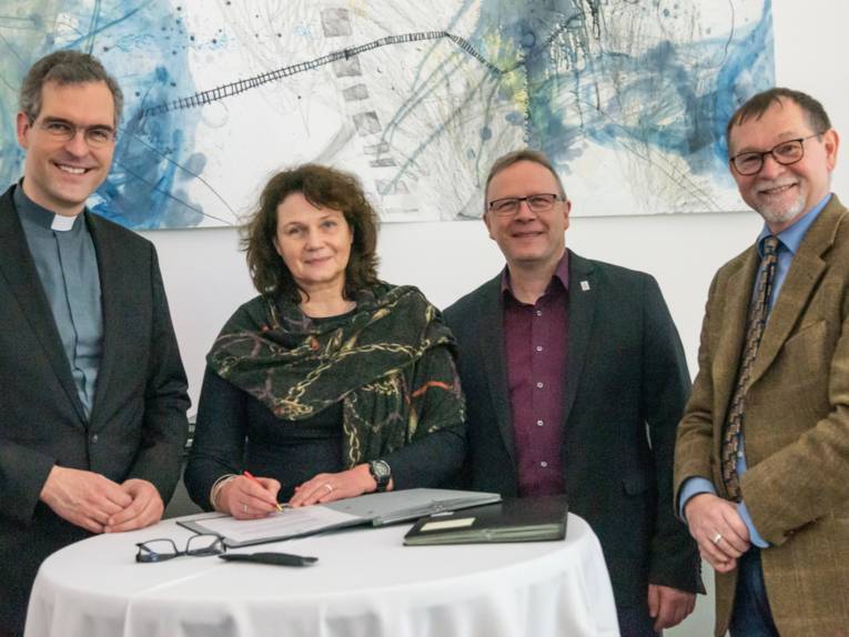 Vier Personen stehen an einem runden Tisch, auf dem Dokumente liegen