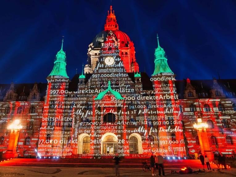 Das Neue Rathaus wird rot angestrahlt, zudem sind Begriffe und Zahlen auf die Fassade projiziert