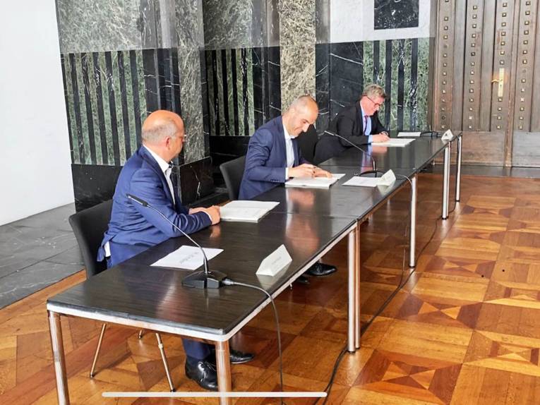 Drei Männer an einem Tisch bei der Unterzeichnung eines Vertrages. 